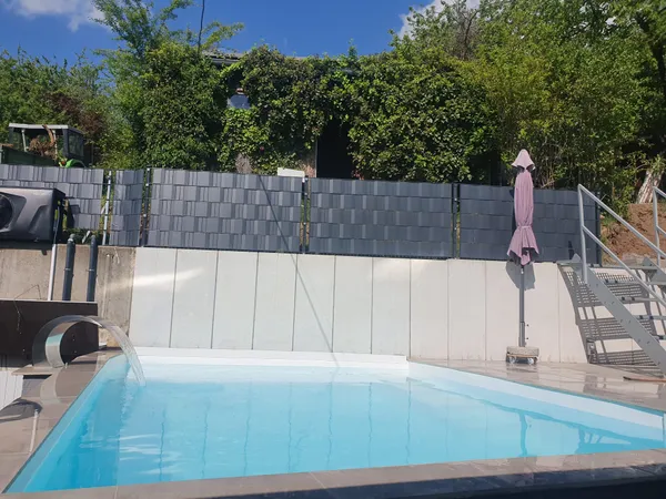 Pool mit Schwalldusche und Zaun auf Stützwand